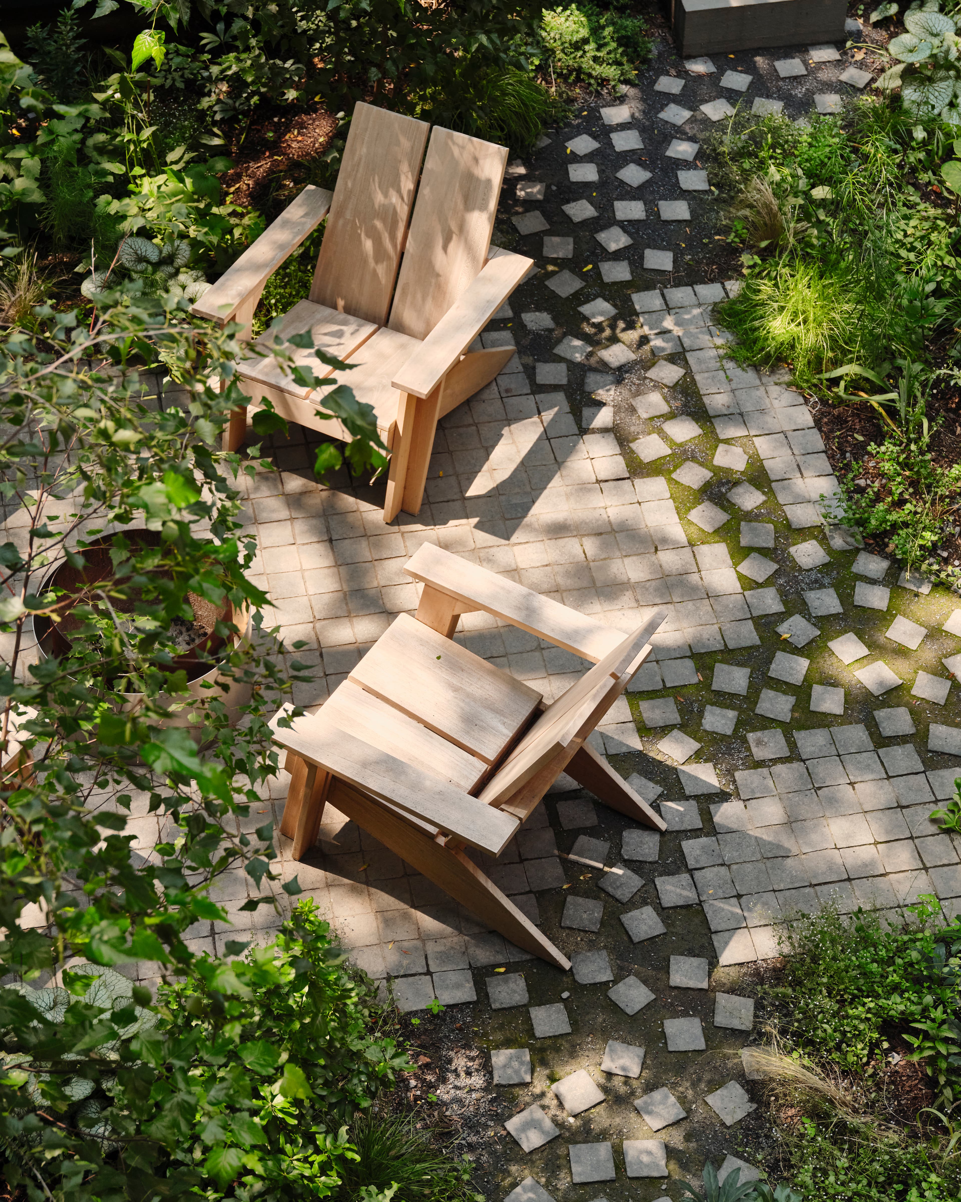 Overhead view of two blond-wood lounge chairs on square basalt cobbles that scatter loose into the planting, echoing the home's square motif