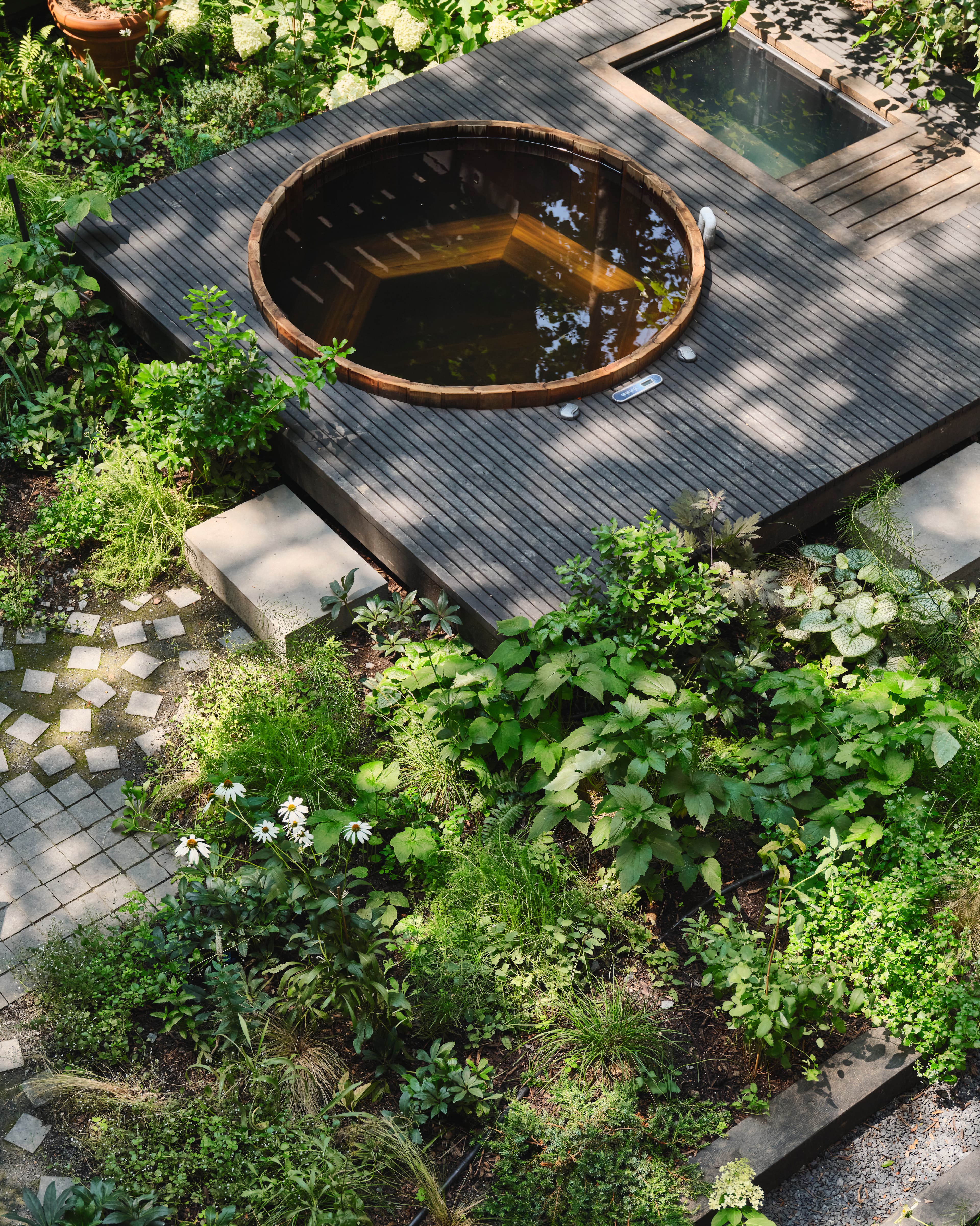 Overhead view of the courtyard deck with a cedar hot tub and cold plunge set among scattered basalt cobbles and dappled, sun-loving planting