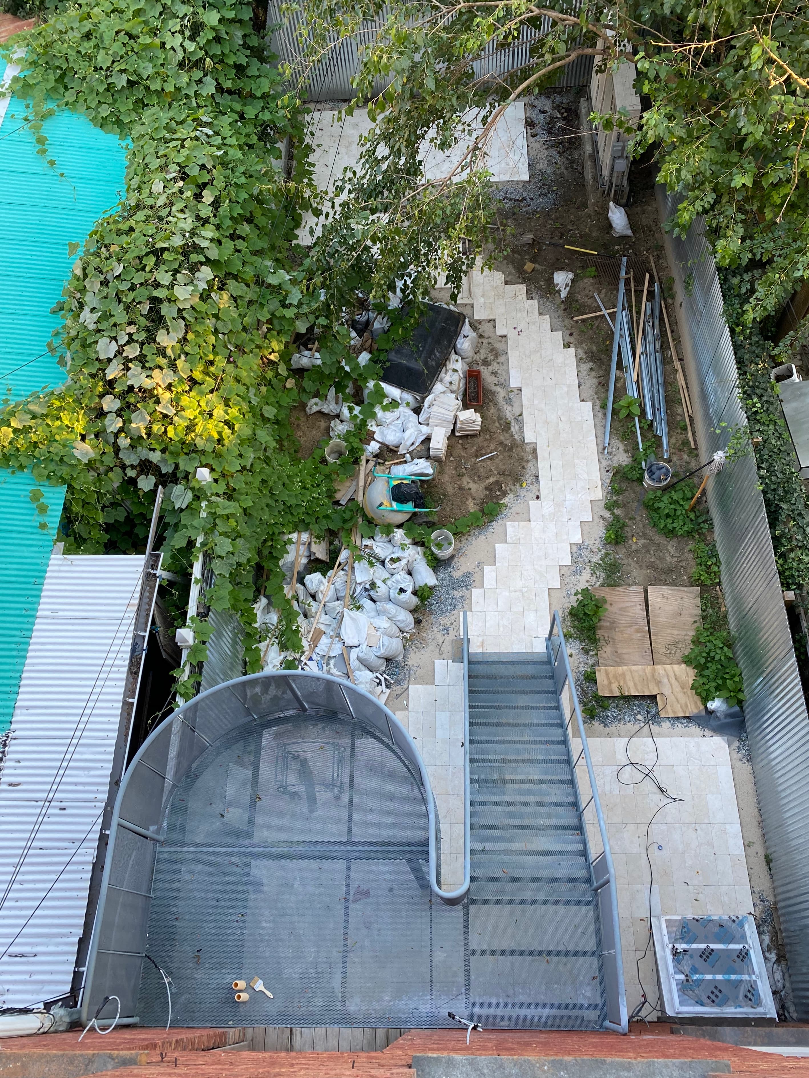Overhead installation shot of the perforated metal stair with limestone paving mid-lay and construction materials staged across the Bedford Stuyvesant yard