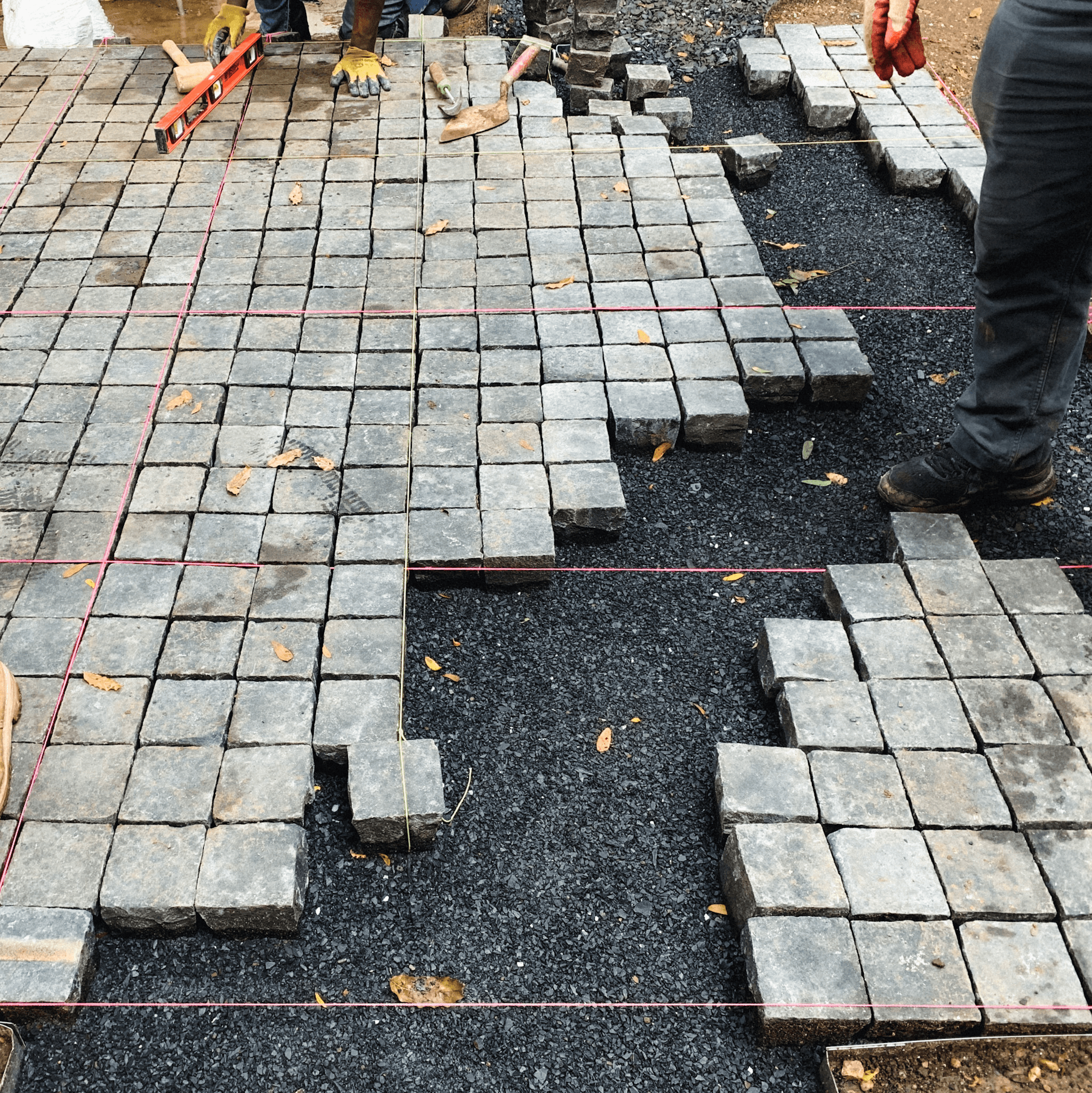 Installation in progress with masons setting square basalt cobbles to string lines over a gravel base